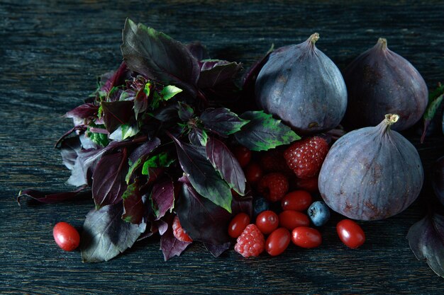 Berries bunch, basil and figs on a wooden dark background