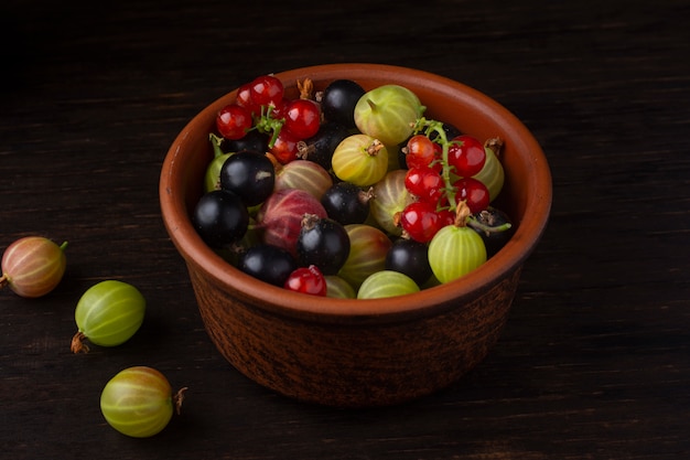 Berries of currant and gooseberry in a ceramic bowl on a dark background