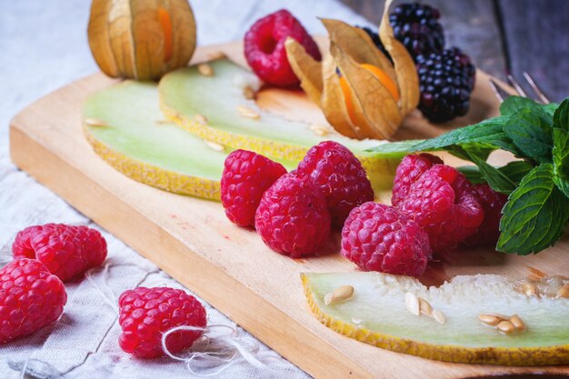 Berries, mint and melon on wooden cutting board