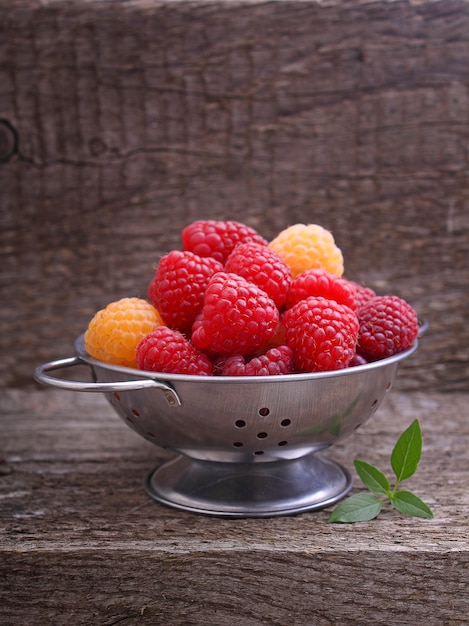 Berries red and yellow raspberries in a metal bowl on a dark wooden background