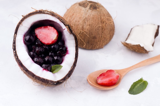 Bacche di fragole e ribes in una metà di cocco su uno spazio bianco. concetto di estate