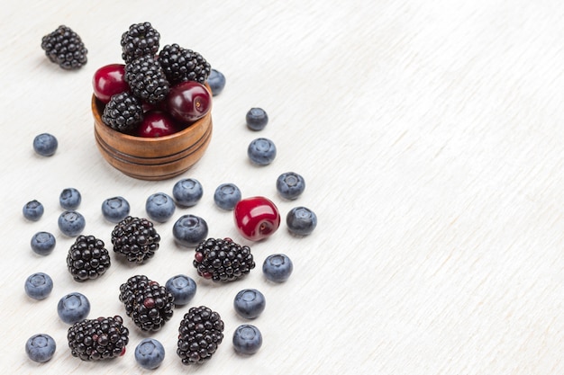 Berries in wooden box and on table: blackberry, cherry, blueberry and raspberry. White surface. Top view. Copy space