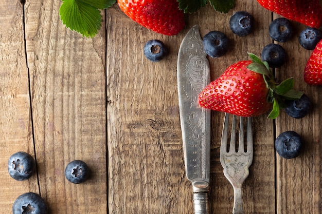 Berriey mix, blueberry, strawberry on wood background with vintage, styled fork and knife. 