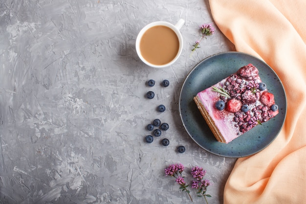 Berry cake with milk cream and blueberry jam on blue ceramic plate with cup of coffee and fresh blueberries.