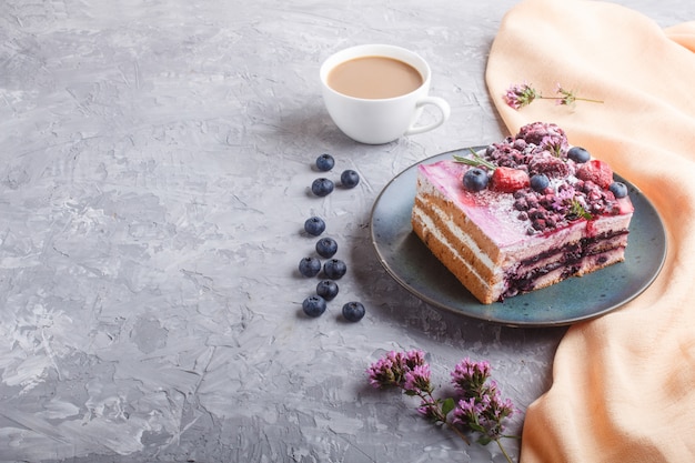 Berry cake with milk cream and blueberry jam on blue ceramic plate with cup of coffee and fresh blueberries.