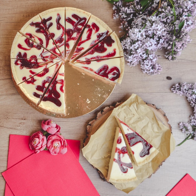 berry cheesecake on a wooden table with lilac flowers around top view