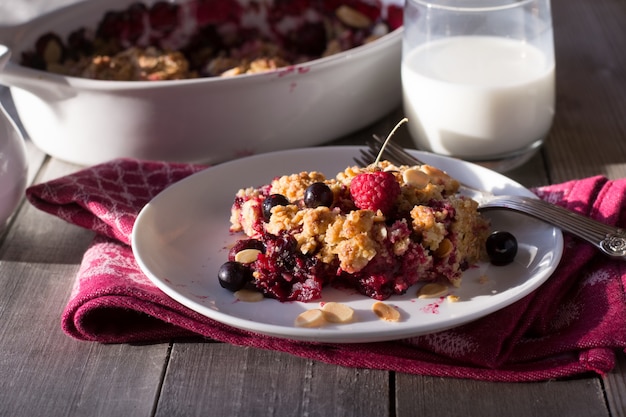 Berry crumble in white plate on grey wooden background.