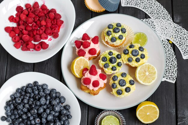 Berry cupcakes with butter cream on black wooden table.