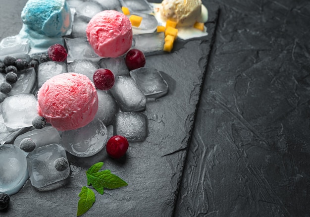 Berry and fruit ice cream on ice on a black wall with space to copy. Side view, horizontal.