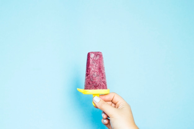 Berry homemade ice cream in a female hand on a blue background