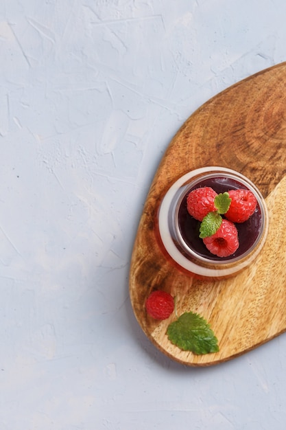 Berry jelly topping with raspberries in a glass cup on a wood stand