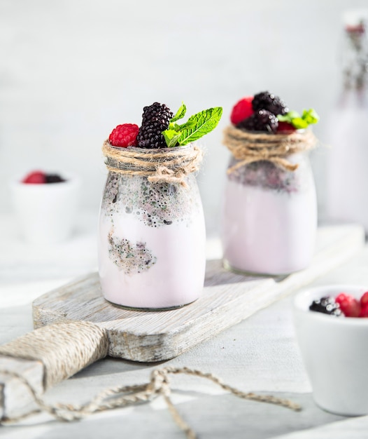 Foto berry milkshake in glazen flessen op witte houten snijplank op wit.