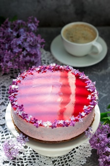 Una mousse ai frutti di bosco con base di cioccolato e gelatina di succo, decorata con fiori lilla, servita con caffè.
