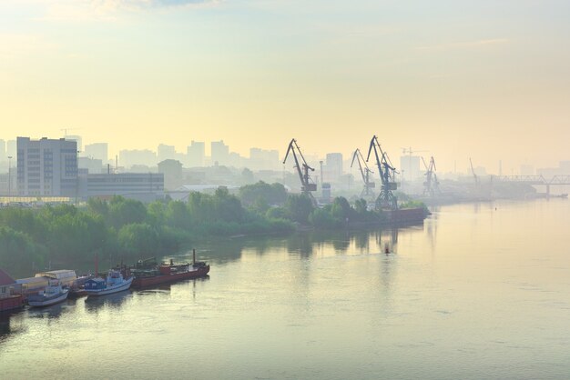 berths and ships on the surface of the water the shore of the city with port cranes in the haze