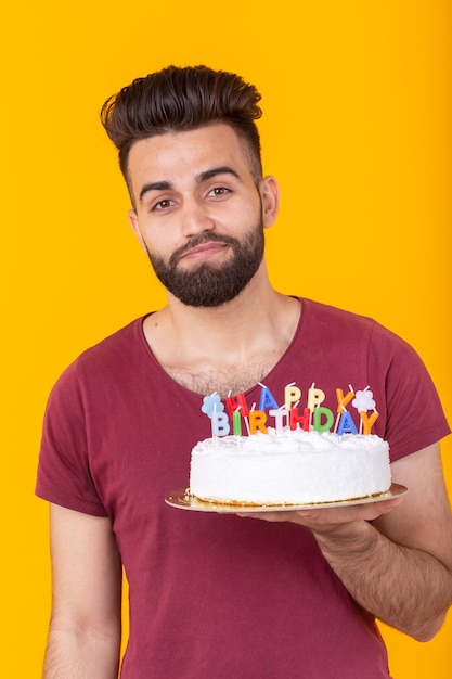 Beschaamd jonge mannelijke hipster met baard met een verjaardagstaart in zijn handen en op zoek