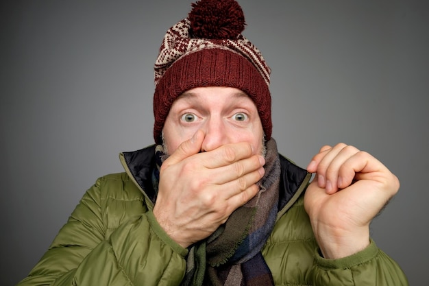 Foto beschaamde geschokte man in warme kleren en sjaal die mond bedekt met handen hij hoorde de weersvoorspelling