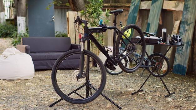 Beschadigde fiets in de tuin in afwachting van reparatie en onderhoud, klaar voor zomerfietsen. Weergave van een moderne fiets die op een reparatiestandaard is geplaatst voor verdere aanpassingen buitenshuis.