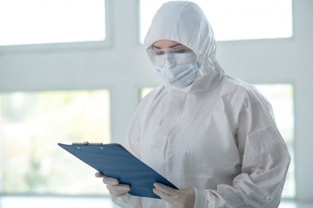 Beschermende maatregelen. Medisch-werker in beschermende kleding, medische masker en bril controleren van iets op clip map