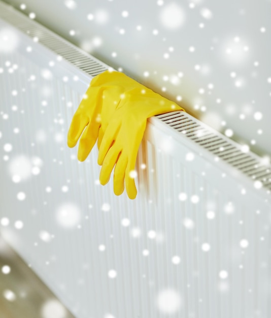 Foto bescherming, huishoudelijk werk en huishoudconcept - close-up van gele rubberen handschoenen die thuis aan de verwarming hangen boven het sneeuweffect