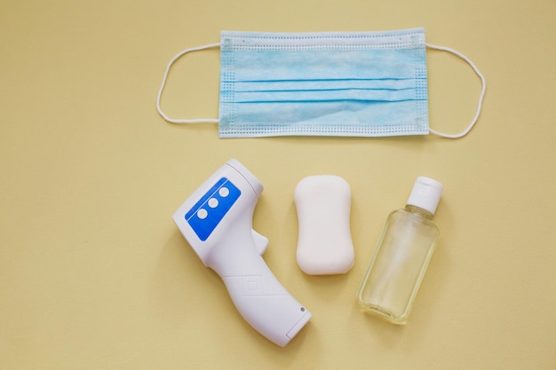 Bescherming tijdens virusuitbraak concept chirurgisch blauw masker zeep handdesinfecterend middel en infrarood thermometer op gele achtergrond