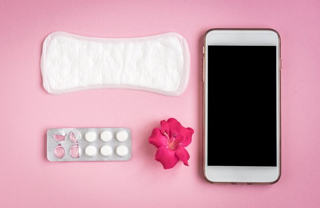 Bescherming van de hygiëne van de vrouw. Maandverband met pijnstiller, roze roos en mobiele telefoon op roze.