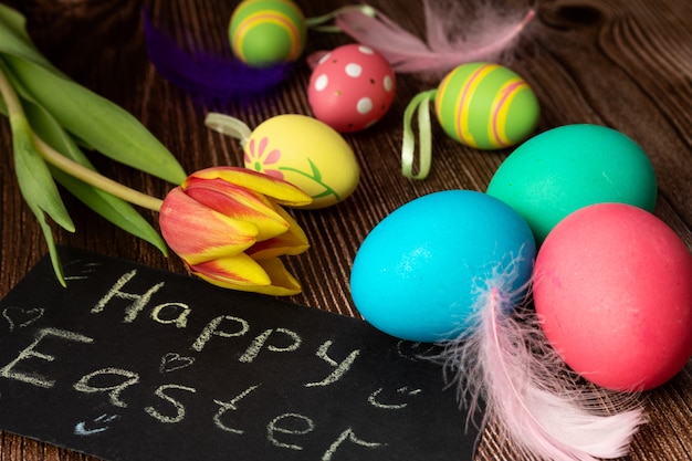 Beschilderde eieren in de buurt van het bord met de inscriptie Happy Easter, veren en tulpenbloem