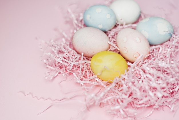 Beschilderde eieren in pastelkleuren op een roze papiervuller en oppervlak.