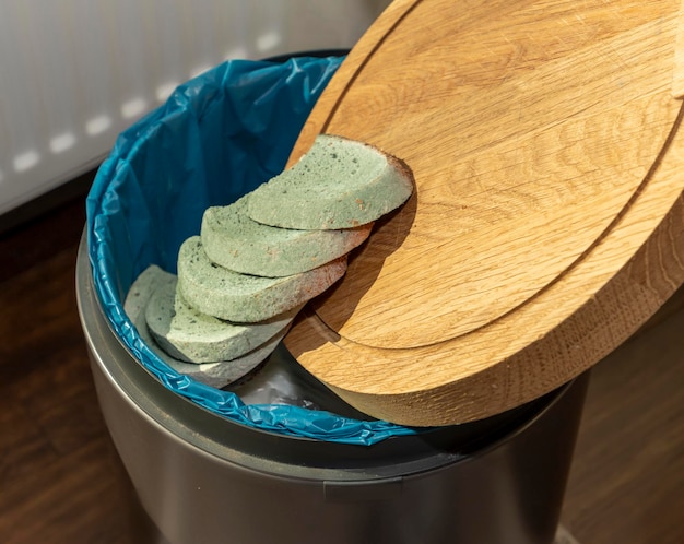 Beschimmeld brood wordt vanaf een snijplank in de prullenbak gegooid