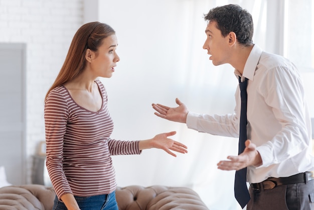 Beschuldigingen. Geïrriteerde emotionele man die naar zijn boze, nerveuze vrouw kijkt terwijl hij de relaties met haar uitzoekt