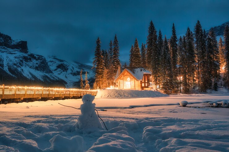 Foto besneeuwd smaragdgroen meer met houten lodge gloeiend in dennenbos en sneeuwpop in de nacht in canada