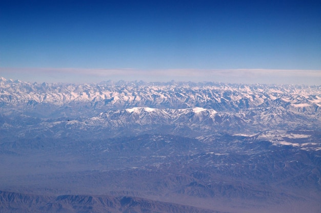 Besneeuwde bergen op blauwe hemel, luchtfoto. Planeet aarde natuurlijk landschap. Reis rond de wereld. Milieubescherming en ecologie. Alleen op aarde is leven mogelijk.