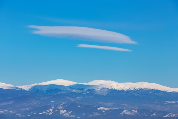 Besneeuwde bergtoppen met naaldbossen en wolken in de blauwe lucht