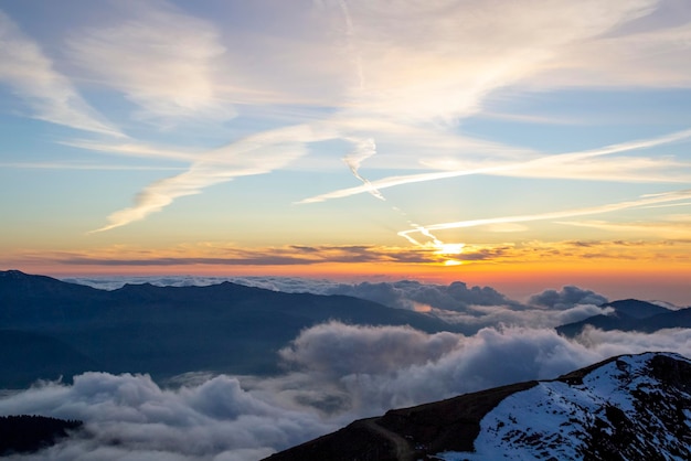 Besneeuwde hoge bergen door de wolken in de blauwe lucht bij zonsondergang