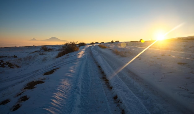 Besneeuwde weg met berg bij de zonsondergang