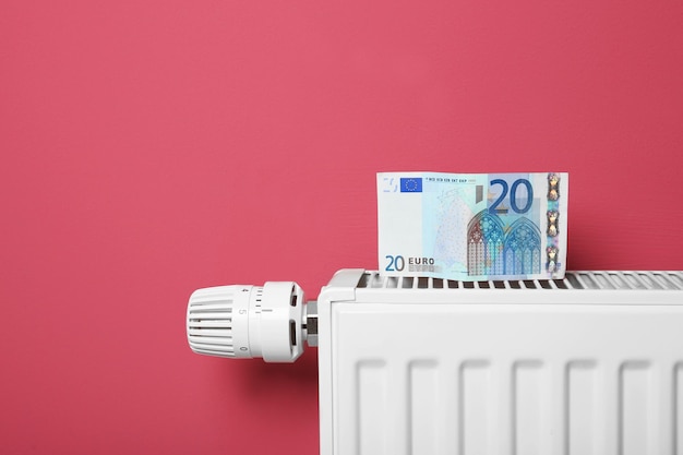 Besparingen concept Geld en verwarmingsradiator met temperatuurregelaar op roze achtergrond