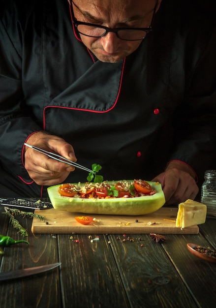 Foto uno chef occhialuto aggiunge il prezzemolo alle zucchine ripiene sul tavolo della cucina il concetto di preparare una zucca o una zucchina ripiena nazionale per pranzo copia spazio