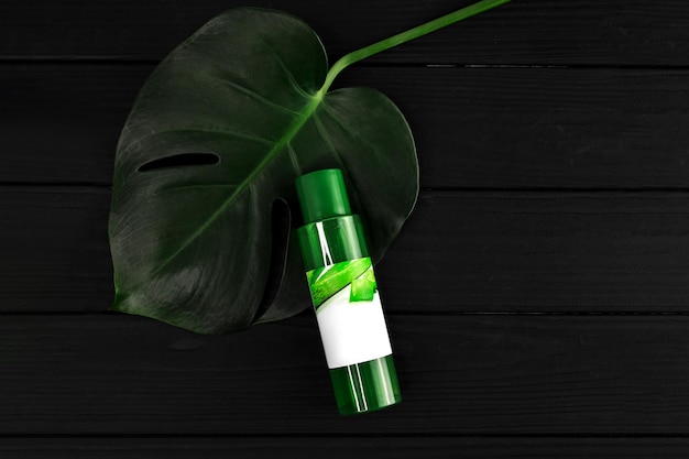 Bespotten groene aloë vera cosmetische container met tropische bladeren op een donkere zwarte houten tafel biologische cosmetica en huidverzorgingsconcept in bottlexdxa