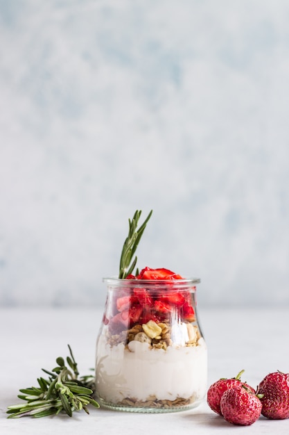 Bessenyoghurt met Griekse yoghurt, verse aardbeien en granola in potten. Gezond ontbijtparfait in glaskop