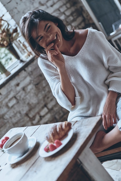 Photo best breakfast! attractive young woman looking away and eating croissant