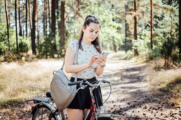 最高のサイクリング アプリ バイク トラッカーの若い女性バックパック自転車に乗って、携帯電話で探しています