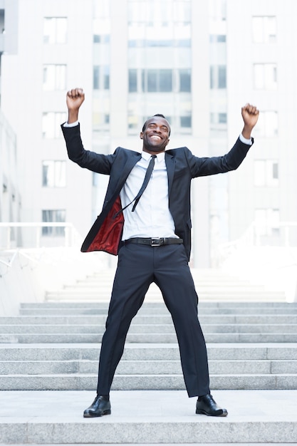 The best day ever! Full length of happy young African man in formalwear keeping arms raised and expressing positivity while standing outdoors