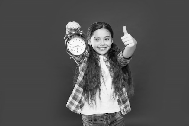 学校の買い物のための休日の時間のための最高の日クリスマスまたは新年の子供へのカウントダウンは、ヴィンテージ時計目覚まし時計で幸せな十代の少女を親指でアラームを聞いています