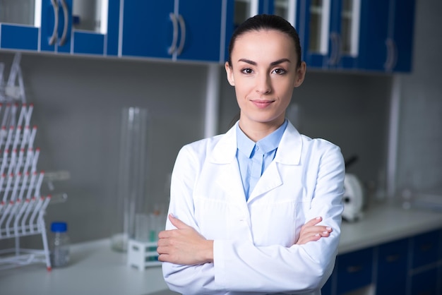 Miglior esperto abbastanza giovane e bella scopritrice in uniforme in piedi in laboratorio sorridendo e tenendo le mani incrociate