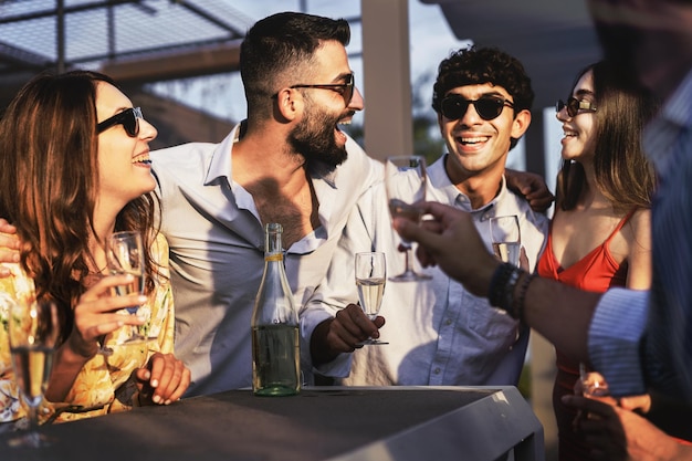 Photo best friends gathering at the outdoor sunset party carefree together talking smiling and joking together drinking sparkling champagne millenials group carefree at weekend standing on bar table