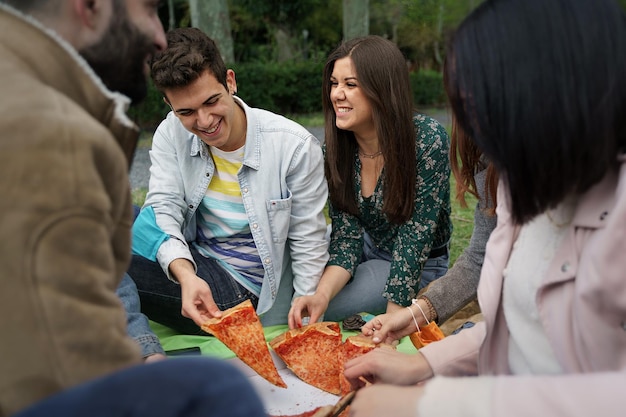 Best friends at picnic eating a sliced pizza sitting on the\
grass of the city park