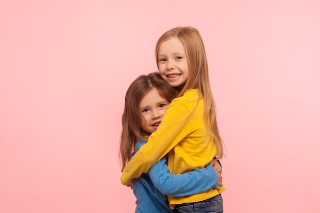 Фото Лучшие друзья с детства портрет двух очаровательных маленьких девочек, обнимающихся и улыбающихся в камеру с беззаботным счастливым выражением лица сестры 39 поддерживают съемку в помещении на розовом фоне