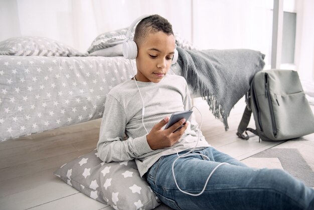 Best playlist. Ambitious afro american boy wearing headphones while looking at phone screen