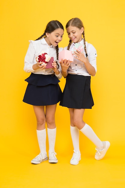 The best presents ever. Surprised little girls opening present boxes on yellow background. Happy children preparing school present for September 1. Small children getting birthday presents.