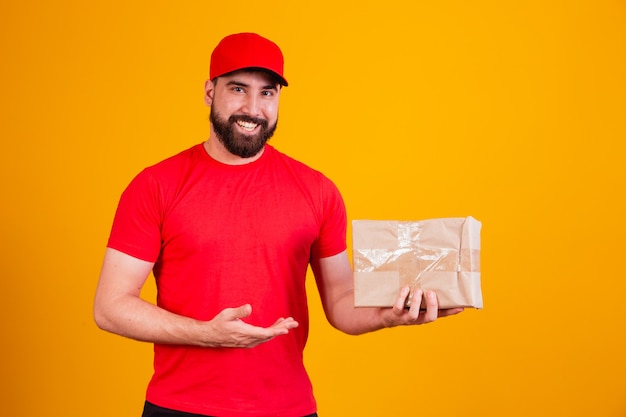 Best Service Concept. Smiling caucasian delivery man in red cap and stacking holding stack of cardboard boxes while standing isolated over yellow studio background. Mail carrying packages