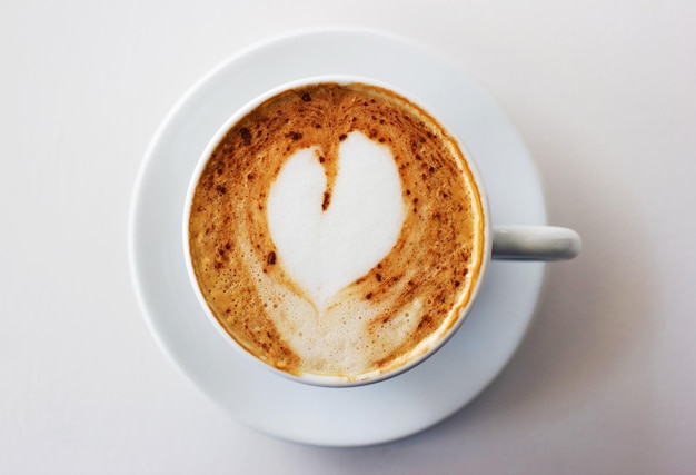 The best start to any morning A freshlymade cappuccino on a white table with a heart shape in the milk froth